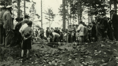 Många personer står vid kanten av en grop som grävs. Linor är bildar avspärrningar.