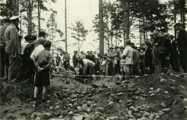 Många personer står vid kanten av en grop som grävs. Linor är bildar avspärrningar.