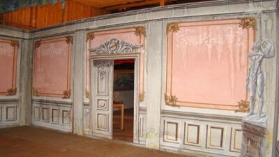En innervägg målad med gråvit panel och rosa väggfält. I mitten en öppen dubbeldörr.
