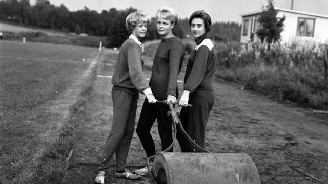 Svartvitt foto föreställande tre unga kvinnor som drar en vält på ett fält. Tidigt 1960-tal.