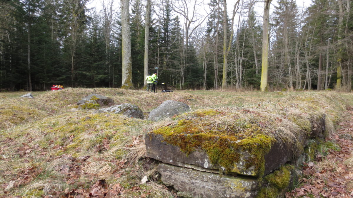 Två personer står i skogen med arkeologisk utrustning.