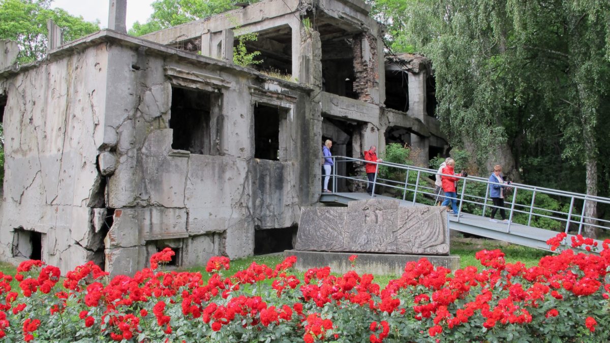 Bild på byggnad med sprickor över väggarna. På gården syns röda blommor.