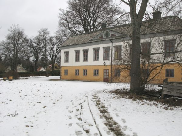 Bild över Rosenlunds herrgård. Snö på marken och stora gamla träd här och där omkring herrgården.