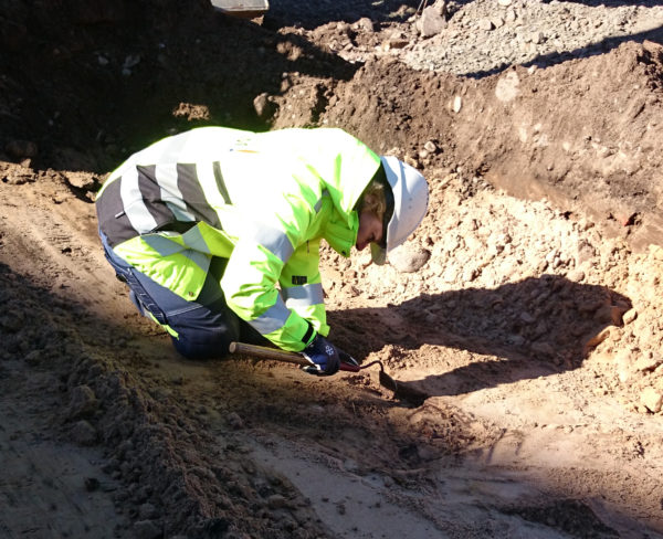 En arkeolog sitter ner och gräver i en grop efter att ha hittat ett något av intresse.