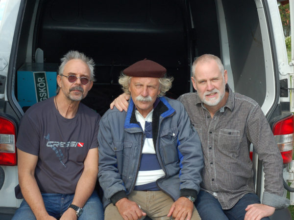 Tre män som sitter på kanten av en skåpbils baggageutrymme.