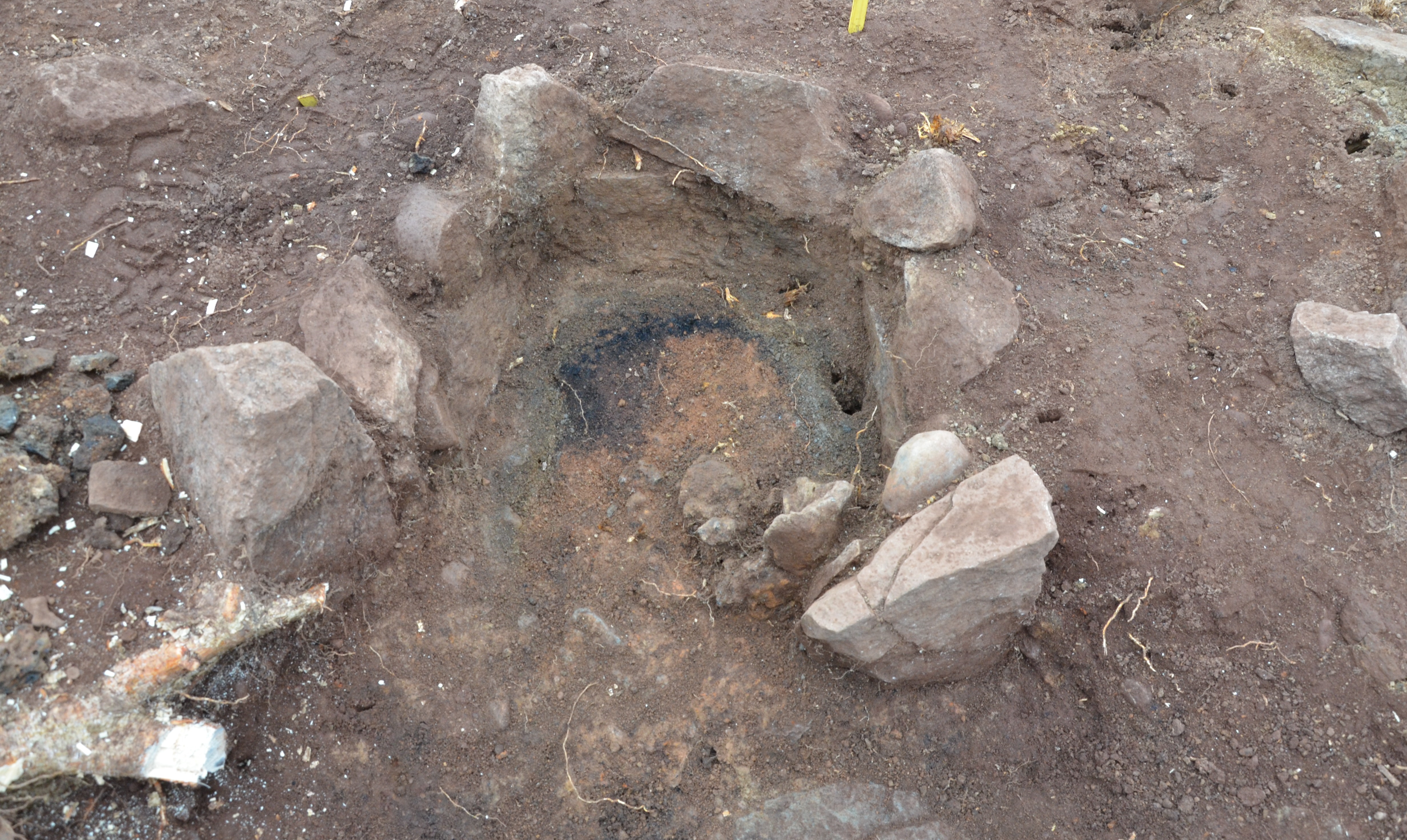 Utgrävning av en ugn med stenar omkring. Svart aska syns i mitten.