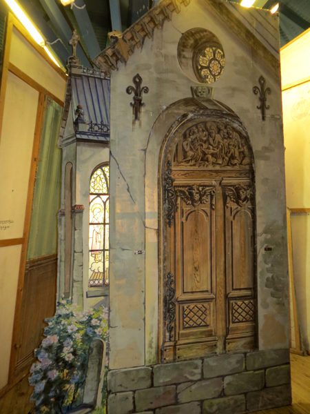 Målad kuliss med kyrk-gavel. Den målade fasaden är grå med detaljer.