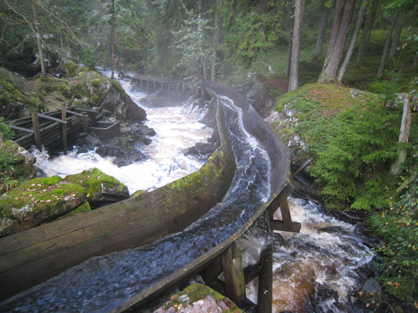 En restaurerad flottningsränna mitt i skogen. I rännan forsar det vatten.