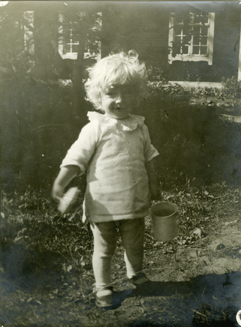 En blond liten pojke står på en stig med en hink i handen.
