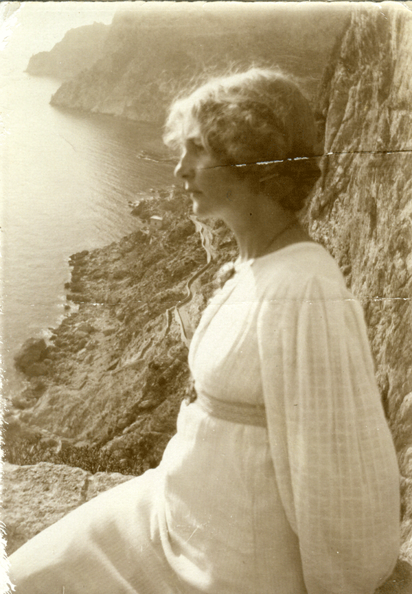 En kvinna med vit klänning sitter på klippor vid ett hav.