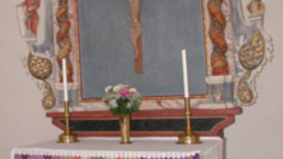 En altaruppsats. Ramen runt har skulpterade människor. I ramen finns ett kors med en man.