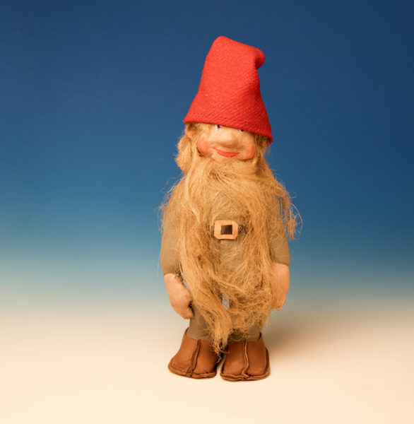 Jultomte-docka med skägg, gråa kläder och röd luva, skärp och skor av skinn.