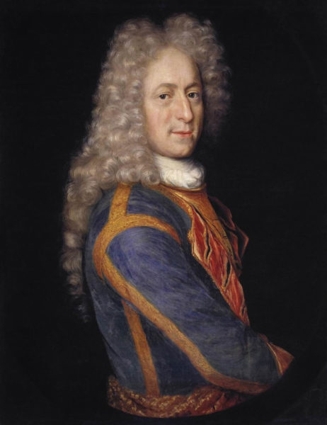 Porträtt av blek man med mörka ögon. Iklädd blå rock med vitt krås. På huvudet stor, krullig och ljusblond 1700-tals peruk.