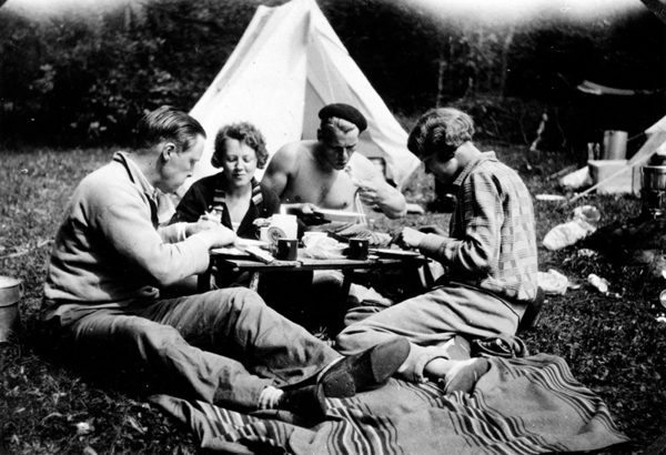 Tältsemester. Två kvinnor och två män sitter framför ett litet tält och äter mat.