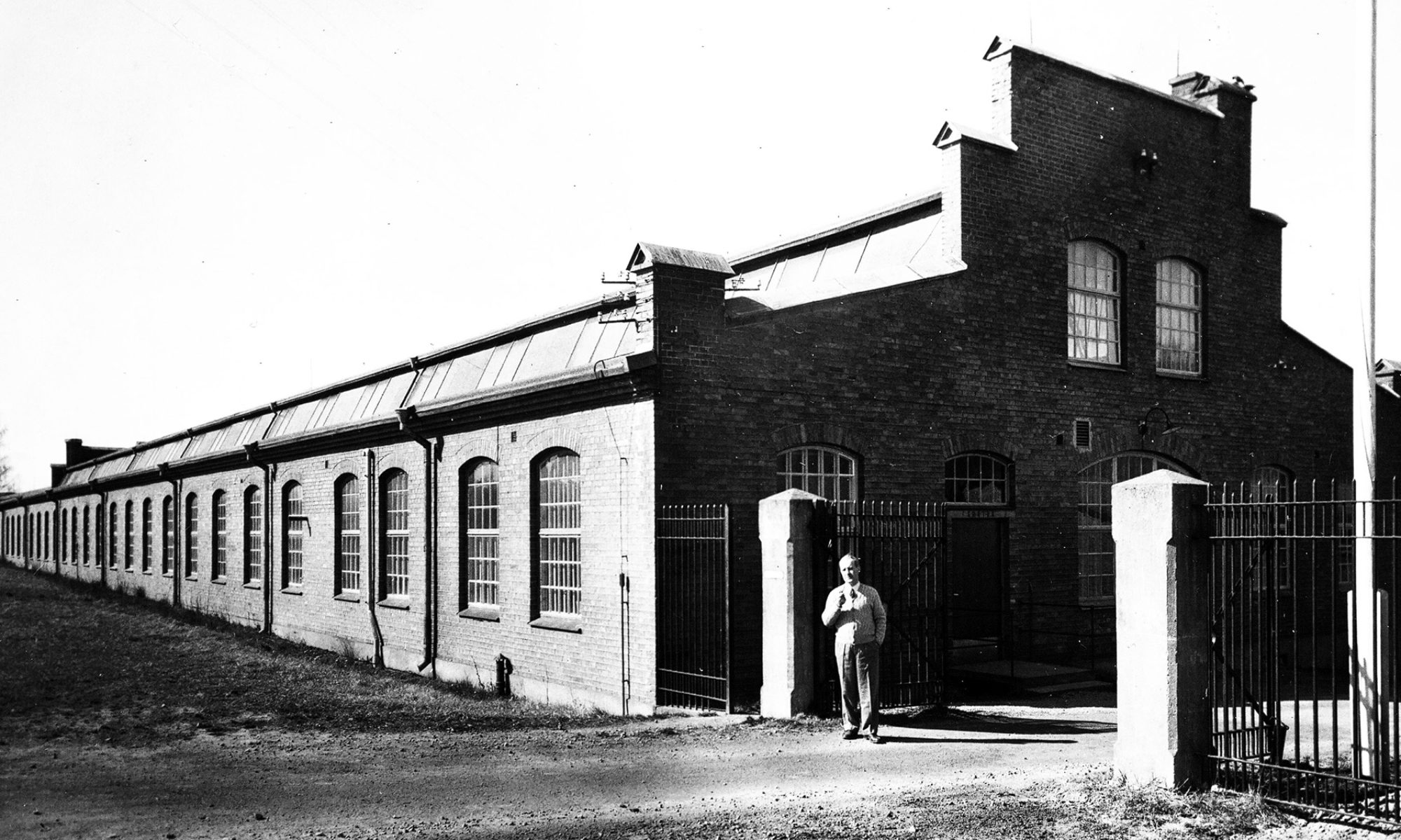 En svartvit bild av en äldre fabrik. En man står framför byggnaden.