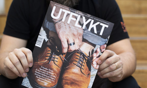 En person håller en tidskrift framför sig. Det står UTFLYKT och är en bild på en man som snörar på sig ett par bruna skor