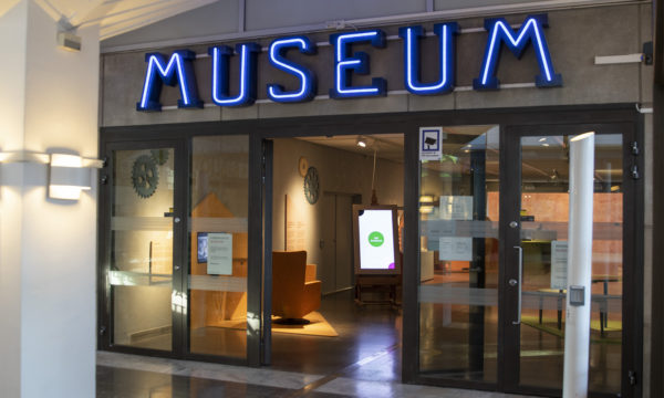 Ingången till museet. Öppna glasdörrar med blåa bokstäver där det står museum ovanför.