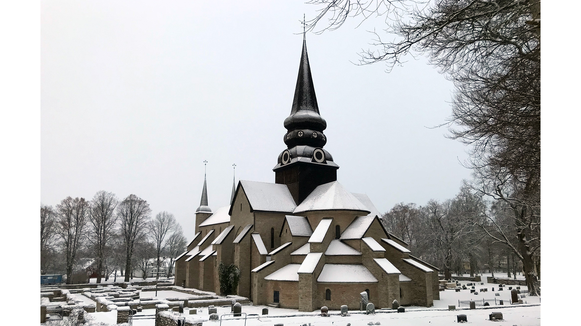 En vintervy över Varnhems klosterkyrka, snö på kyrkan och marken, samt delar av kyrkogården runtomkring syns