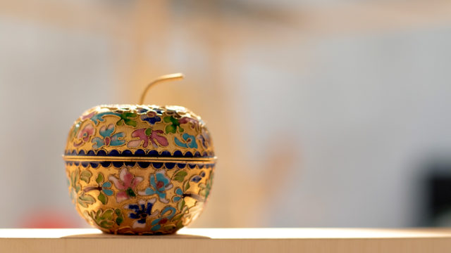Ett äpple i guld täckt av emaljblommor i olika färger som mönster