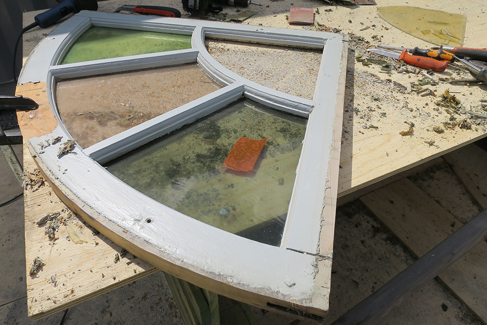 Ett solfjäderformat fönster från en kyrka ligger på en bänk för renovering