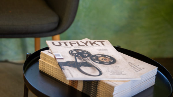 En tidskrift ligger på ett bord i svart metall. I bakgrunden en grön vägg och kanten av en stol.