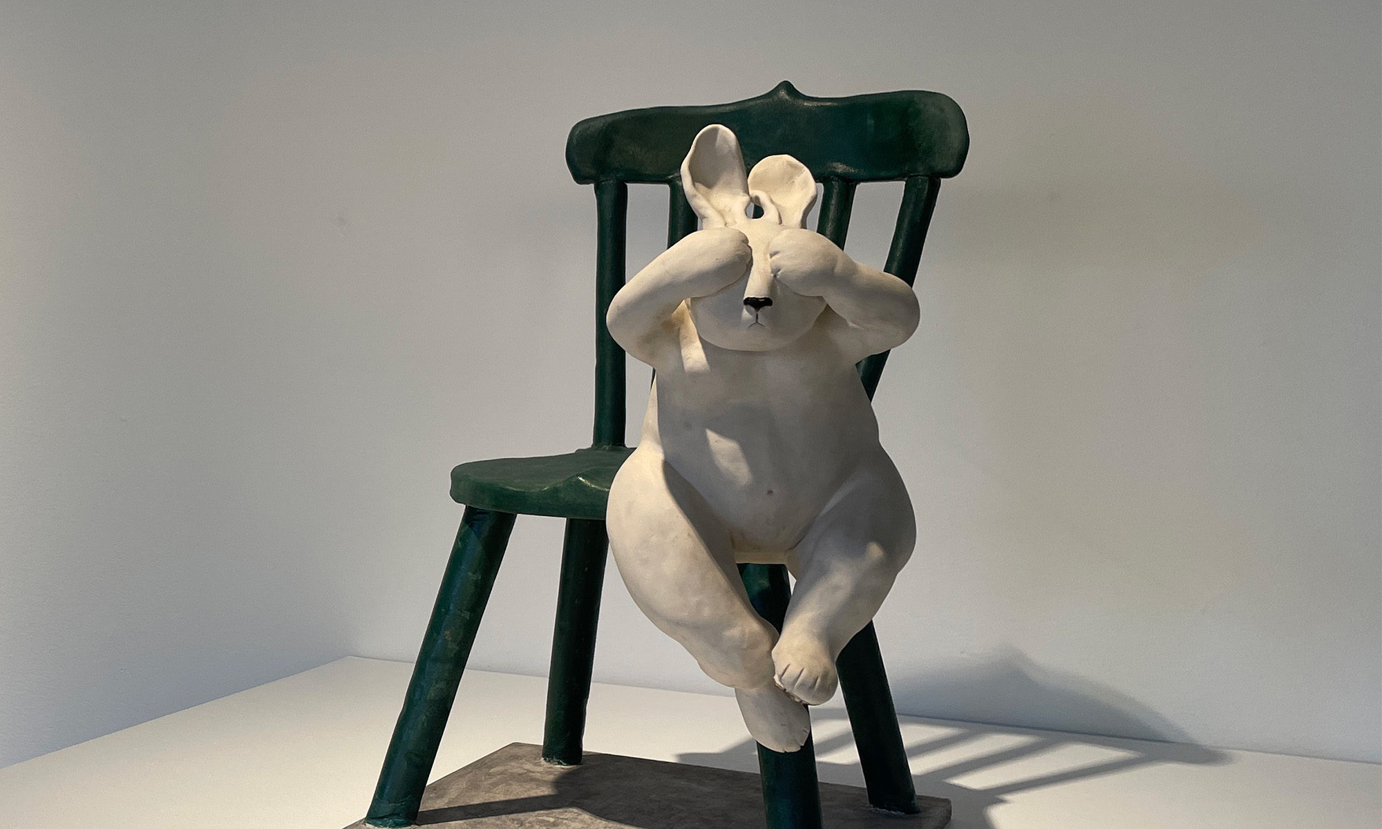 Konstverk föreställande en vit kanin som hoppar från en grön stol i trä