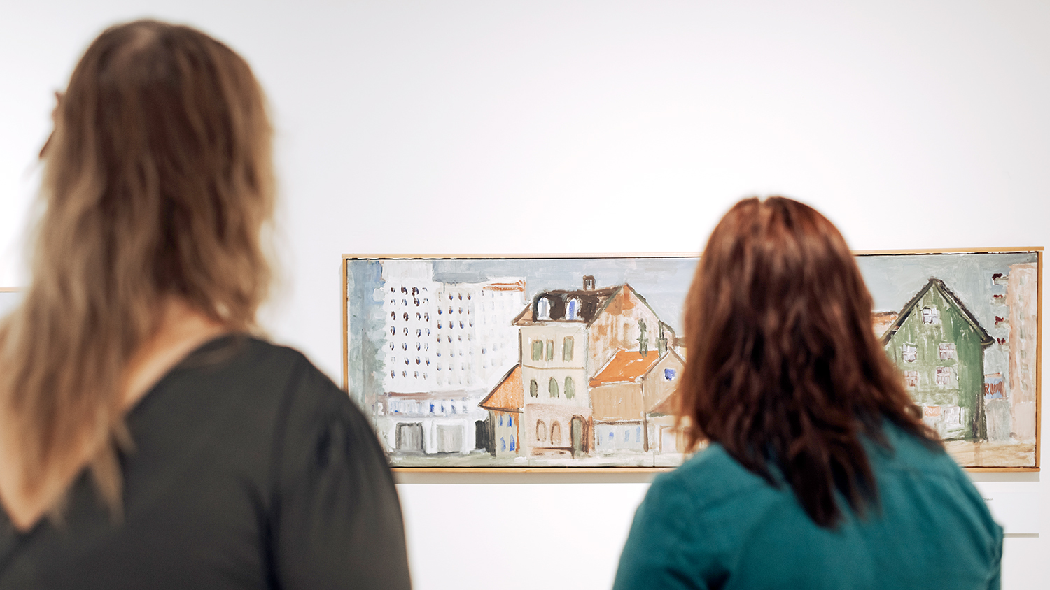 Två personer halvt suddiga i förgrunden, tittar på en målning föreställande äldre hus