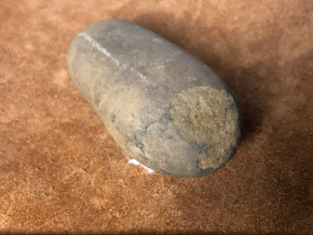 En ovalt formad sten. Rundad och man ser att den har använts för att stöta/knacka då den är sliten i ena änden.