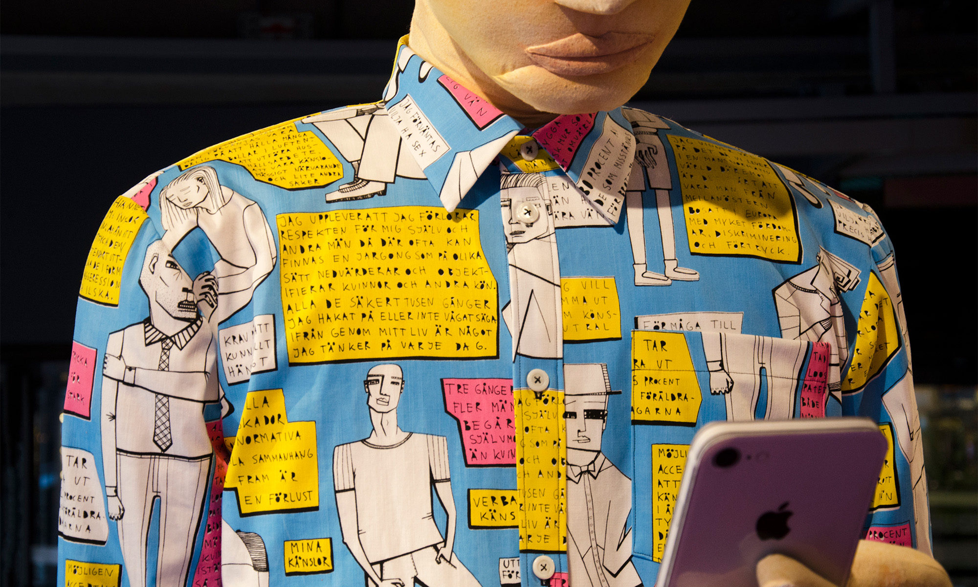 Stor figur med färgglad skjorta med text tryckt på. Figuren håller i en mobiltelefon