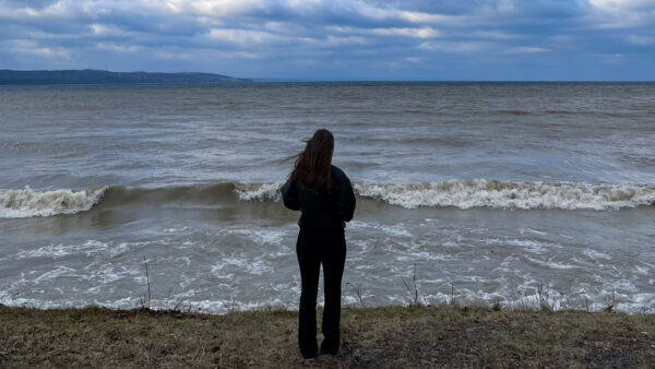 Person med händerna i fickorna blickar ut över vågor på en sjö