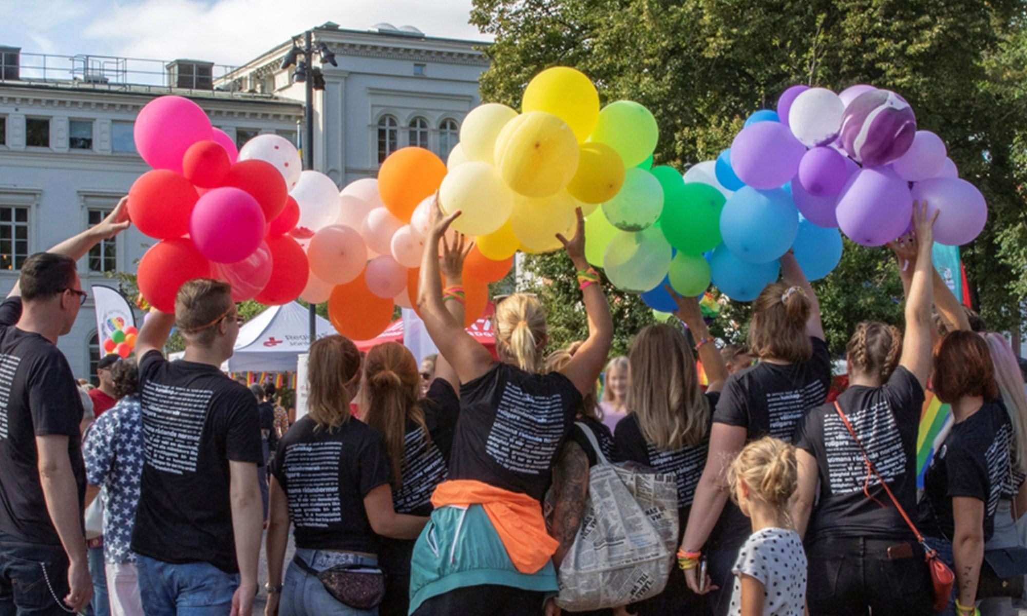 Personer med mörka tröjor håller upp färgglada ballonger ovanför huvudet