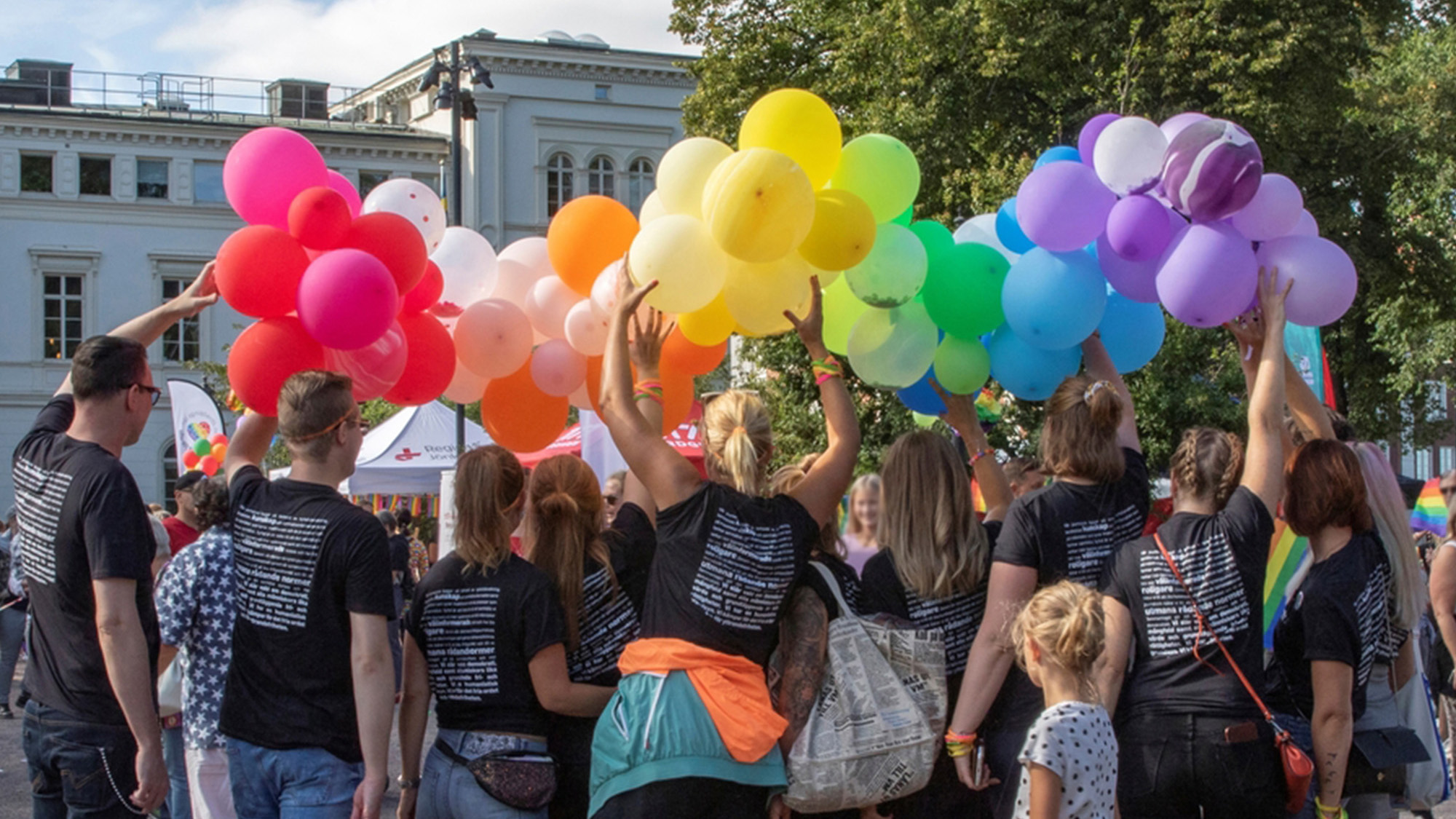 Personer med mörka tröjor håller upp färgglada ballonger ovanför huvudet
