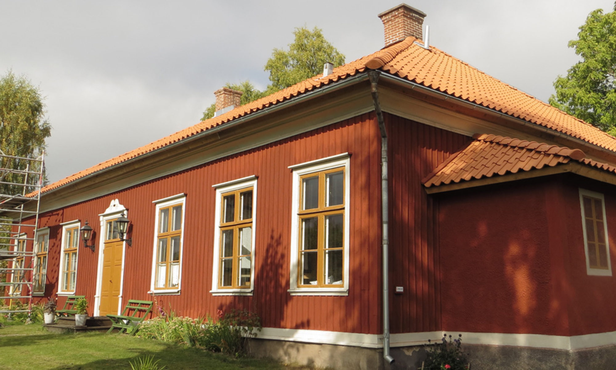 En rödmålad byggnad med gulorange fönsterfoder och dörr