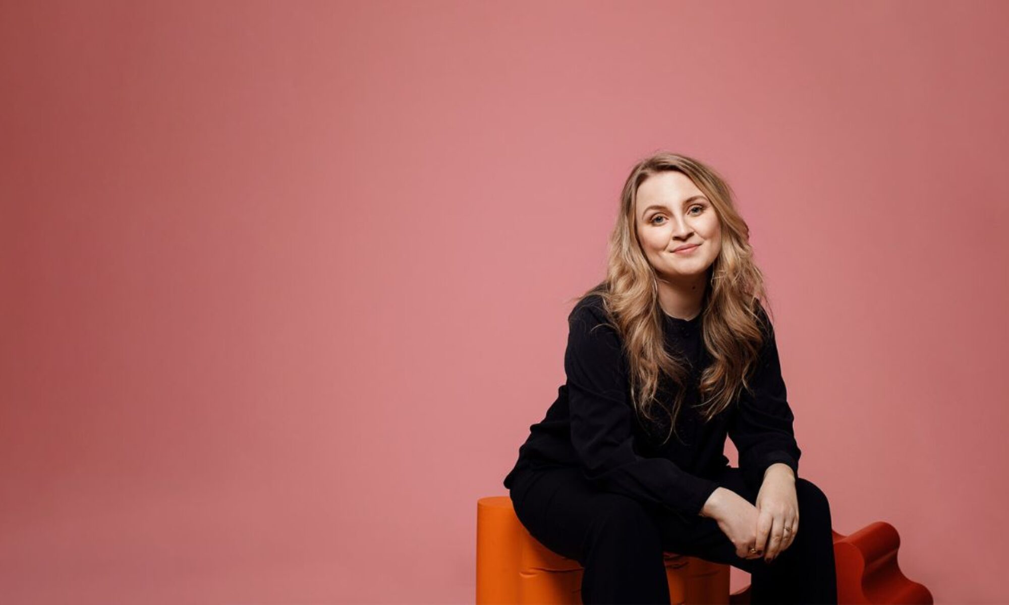 Irena Pozar sitter på en pall framför en rosa vägg.
