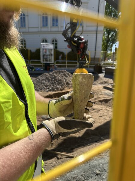 Person med skägg och varselkläder håller upp en kilformad sten