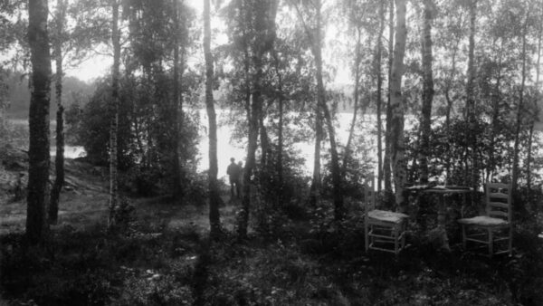 Svartvitt foto av John och Ester Bauer som står i en skog. Två stolar i förgrunden