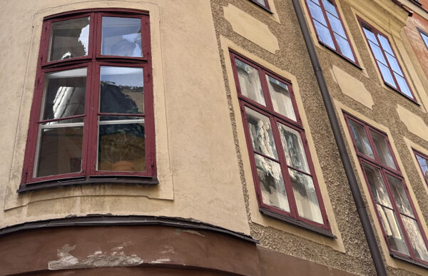 Äldre byggnad med ursprungliga fönsterbågar, vilka är rödmålade och med böljande munblåst glas i dem. 